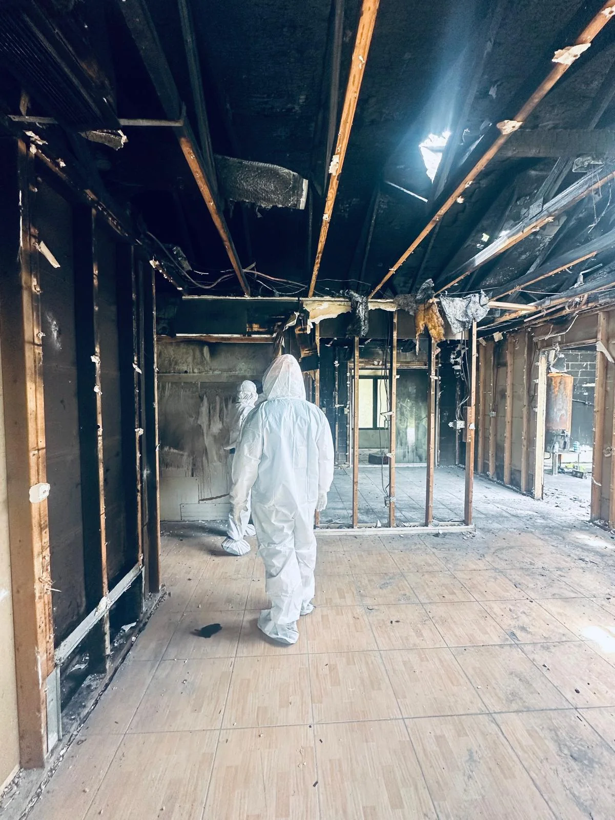 Worker in protective clothing walking through exposed fire-damaged framing