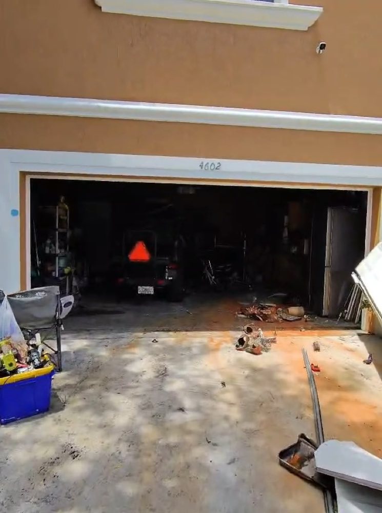 Open garage with equipment and debris in the driveway