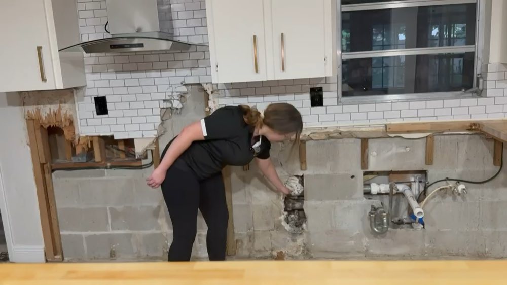 Person pointing to exposed plumbing in a kitchen