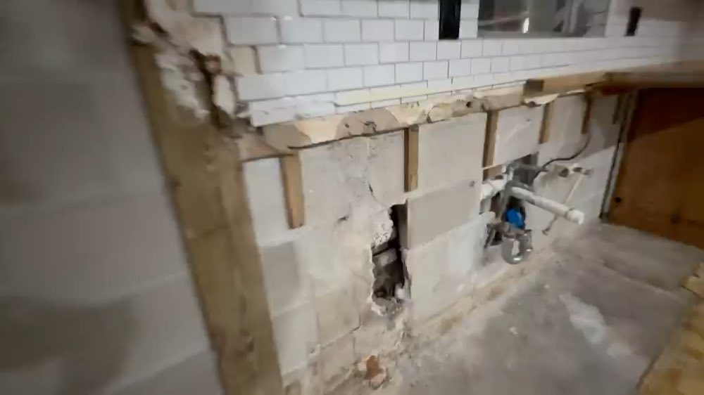 Exposed plumbing and blockwork beneath a tiled kitchen wall